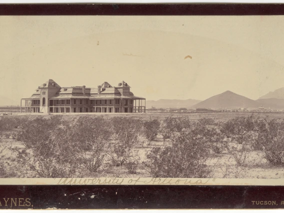 Desert landscape creosote bushes in foreground with background of French colonial style historic two story building with wrap around verandas built in 1891