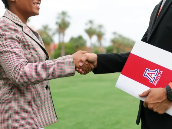 Two individuals shaking hands with a University of Arizona agreement folder