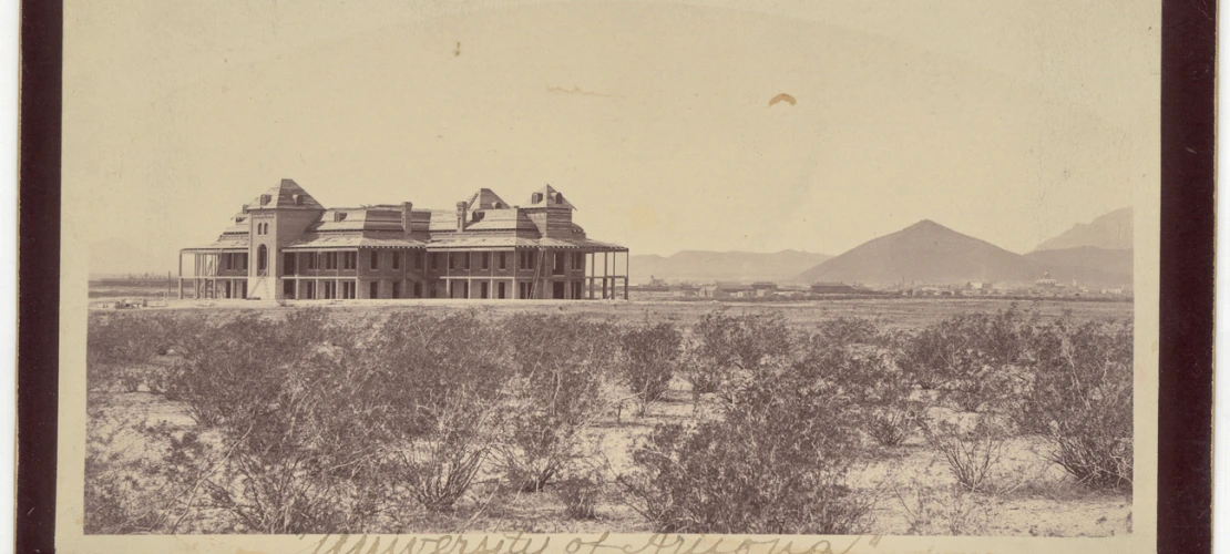 Desert landscape creosote bushes in foreground with background of French colonial style historic two story building with wrap around verandas built in 1891