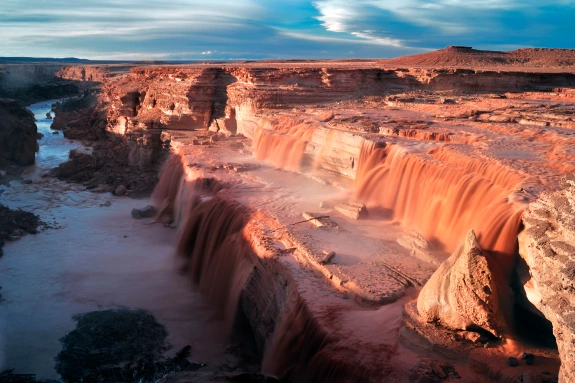arial view of a muddy waterfall flowing into a canyon