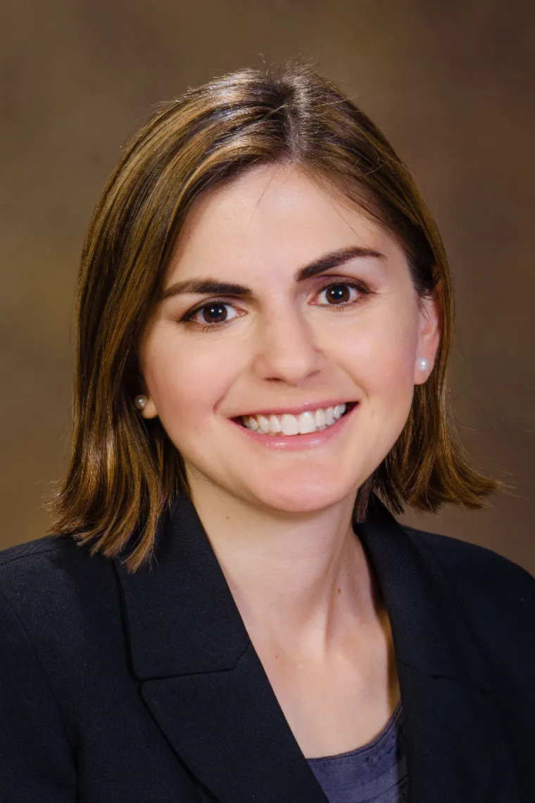 Woman with shoulder length brown hair smiling, black blazer, navy blue top