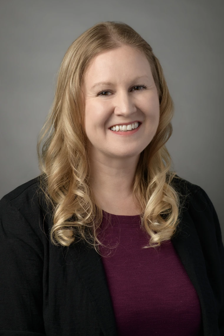 Image of woman with long blonde hair, burgundy top, and black jacket smiling at camera