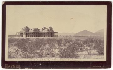Desert landscape creosote bushes in foreground with background of French colonial style historic two story building with wrap around verandas built in 1891